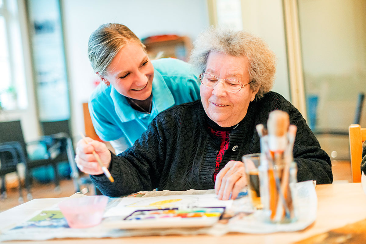 Zwei Personen sitzen an einem Tisch, eine Malt
